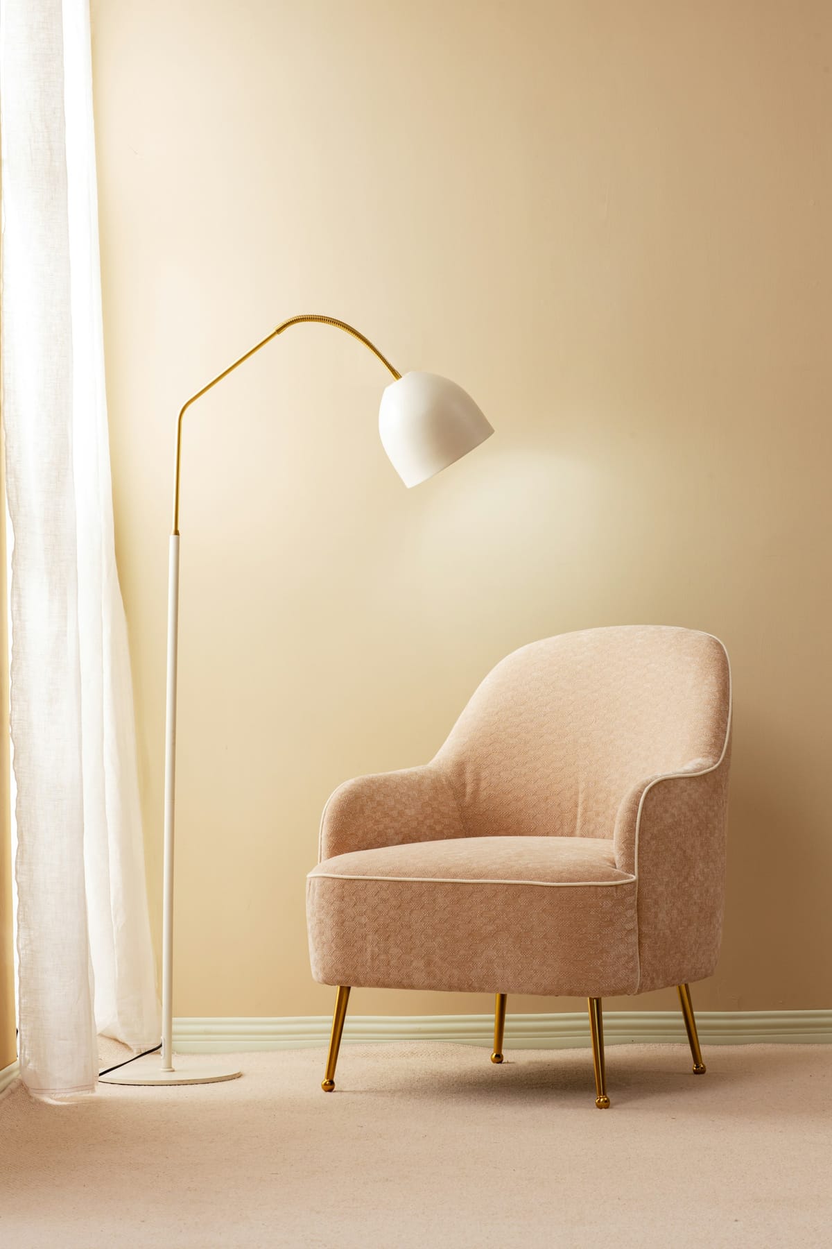 A soft blush armchair beside an arc floor lamp in a warm, cream-colored corner